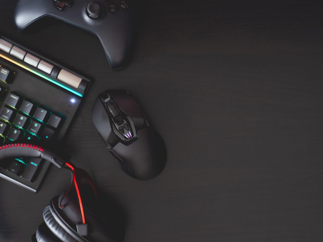 gamer work space concept, top view a gaming gear, mouse, keyboard, joystick, headset, mobile joystick, in ear headphone and mouse pad on black table background.